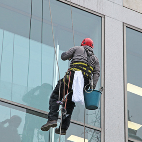 Eine Reinigungskraft säubert die Außenflächen der Fenster eines mehrstöckigen Gebäudes